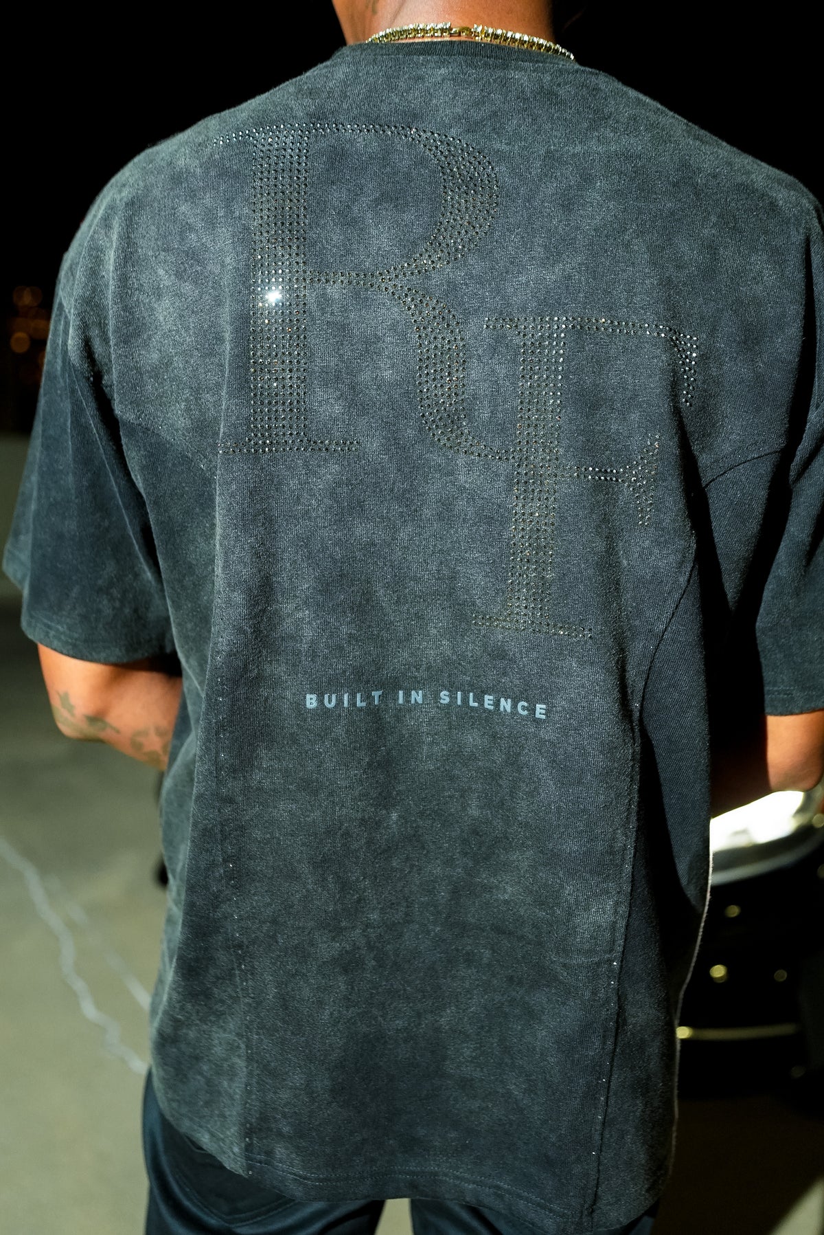 Silent Construct Signature Tee — back close-up of the black rhinestone RF and BUILT IN SILENCE detail, worn.