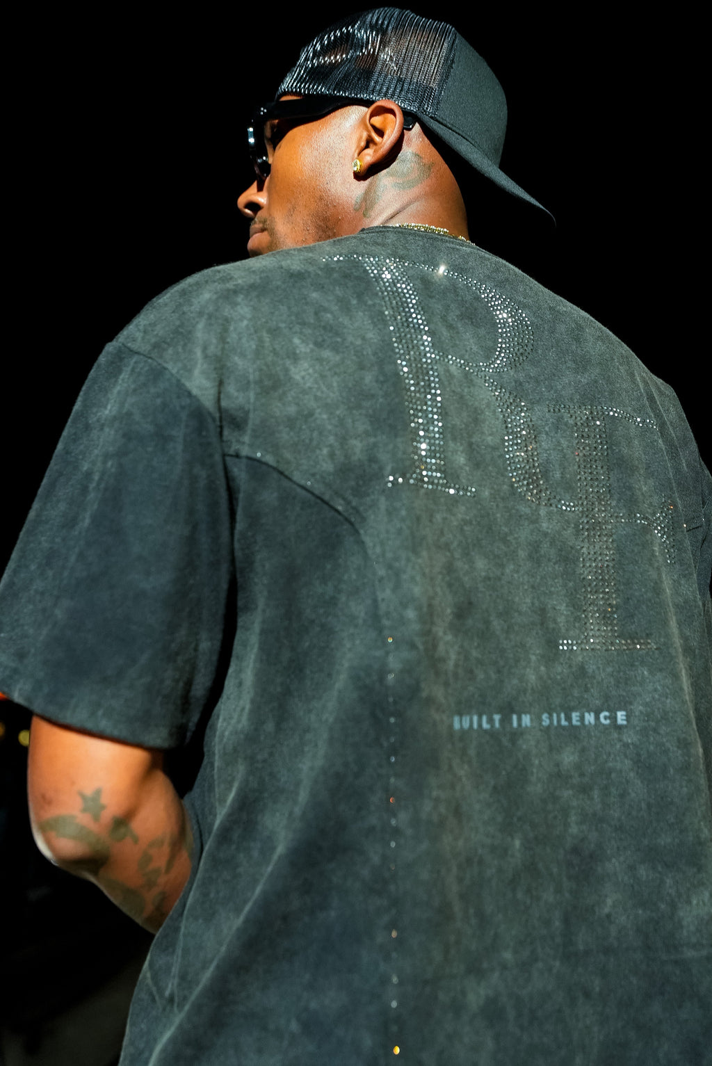 Silent Construct Signature Tee — back three-quarter model shot showing rhinestone RF and oversized fit.