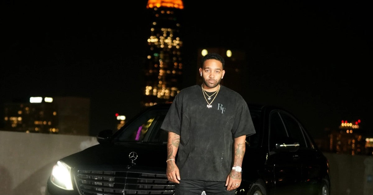 Silent Construct Signature Tee — editorial social share image, model in the washed-black tee with black Mercedes and Atlanta skyline at night. BUILT IN SILENCE.